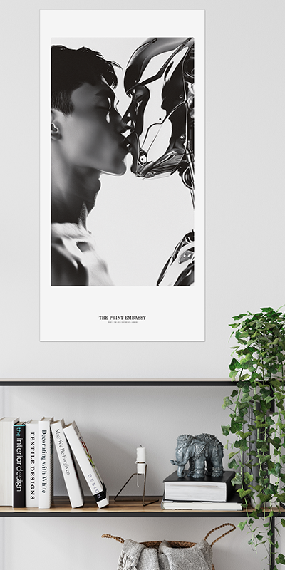 A modern black and white 50x100cm oversized print showing a close-up of a man kissing a robot with 'The Print Embassy' branding below. The poster is hanging on a wall above a modern bookshelf with plants and an elephant statue. 