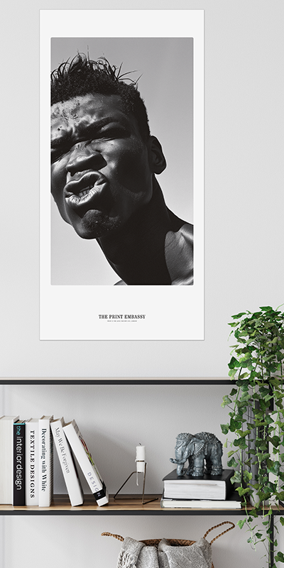 Black and white portrait of a person pulling a funny face, on a wall above a shelf with books and decor.