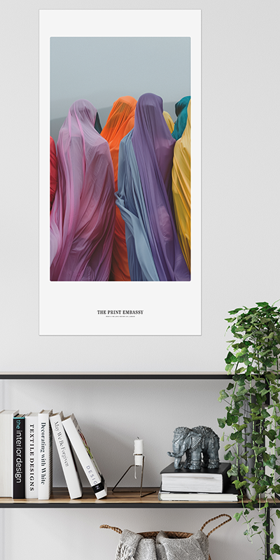 A group of people facing away from the camera wearing very colorful burqas. They are looking out towards a beautiful foggy and hilly expanse. The large unframed print is by The Print Embassy. The oversized artwork is displayed on a wall above a bookshelf.