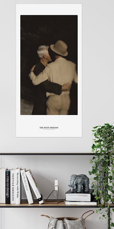 Framed artwork of a male couple embracing above a shelf with books and decor. Love is love, at any age.