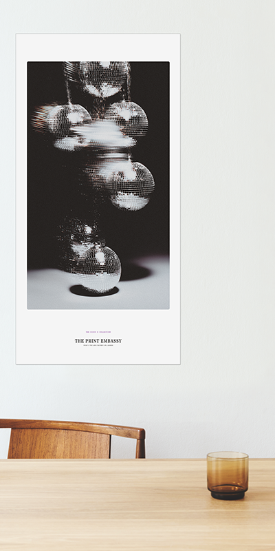 Poster of disco balls on a wall above a wooden table with a glass vase. The large wall poster is from The Print Embassy Disco X Collection.