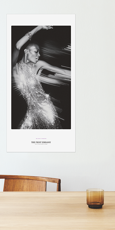 Poster of a woman in a sparkling dress on a wall above a wooden table with a glass.